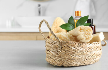 Natural loofah sponges in wicker basket on table indoors. Space for text