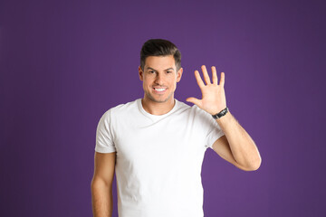 Man showing number five with his hand on purple background