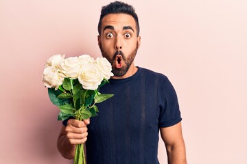 Young hispanic man holding flowers scared and amazed with open mouth for surprise, disbelief face