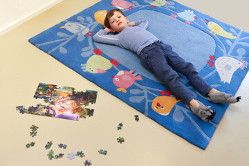 Ein kleiner Junge liegt gelangweilt auf einem Kinderteppich
