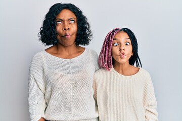 Beautiful african american mother and daughter wearing casual clothes and hugging making fish face...