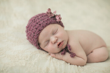 Serene sleeping newborn baby girl with a purple crochet hat on her head curled up on a cream-colored blanket