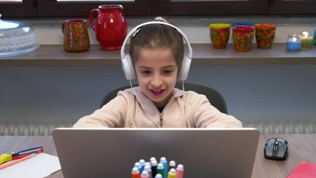 Little girl studying with laptop pc. Sad female student learning with computer. Bored child doing school homework and e-learning during coronavirus pandemic. Remote education at home
