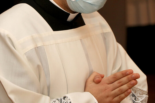 Young priest with hands folded in prayer wears surgical mask due to the Covid-19 pandemic