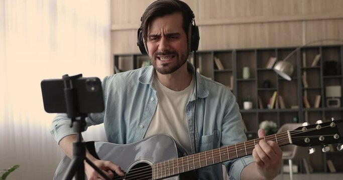 Guitarist wear headphones singing song playing a guitar record video to smartphone gadget. Blogger create tutorial lesson for beginners, string instrument class for internet auditory, hobby concept