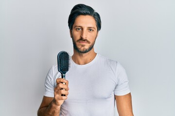 Young hispanic man styling hair using comb thinking attitude and sober expression looking self confident