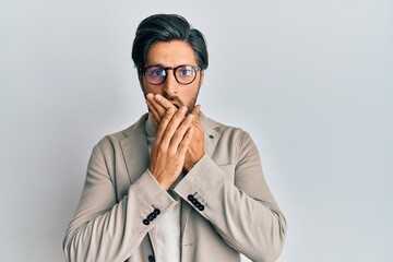 Young hispanic man wearing business jacket and glasses shocked covering mouth with hands for mistake. secret concept.