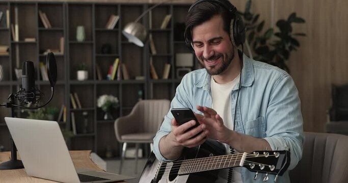 Male guitar player sit indoor with smart phone, take break resting from playing string instrument using cellphone smiles read pleasant message. Hobby, pastime, modern wireless technology user concept