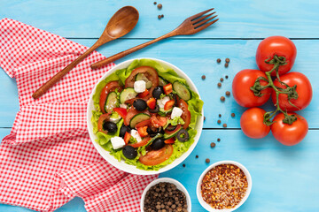 Homemade freshly prepared Greek salad on a blue background with a variety of seasonings. Top view.