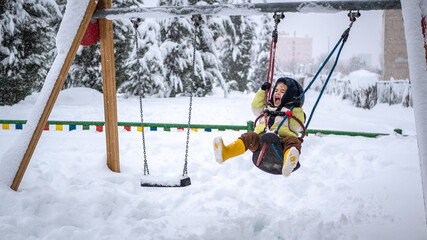 Fototapeta na wymiar A young child boy is enjoying snow outdoors on a playground in Madrid during the heavy snowfall due to Filomena storm in Spain