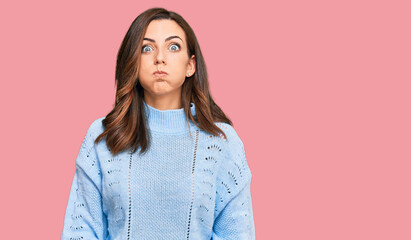 Obraz premium Young brunette woman wearing casual winter sweater puffing cheeks with funny face. mouth inflated with air, crazy expression.