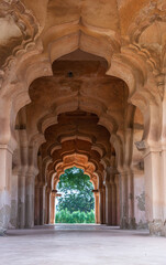 Hampi, Karnataka, India - November 5, 2013: Zanana Enclosure. Looking through a tunnel of arches in Lotus Mahal. Brown stone ending on green foliage. Natural light 
