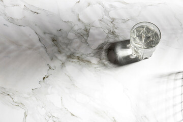 A glass of cold water casting a shadow in hot weather on a marble table.