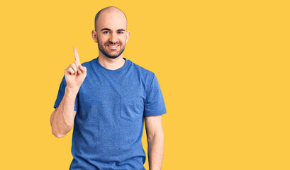 Young handsome man wearing casual t shirt showing and pointing up with finger number one while smiling confident and happy.