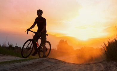 Silhouette of cyclist riding on a dust trail at sunset background.