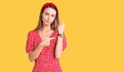 Young beautiful girl wearing dress and diadem in hurry pointing to watch time, impatience, looking at the camera with relaxed expression