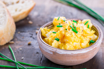  Fresh scrambled eggs with chives in a clay bowl on a wooden table