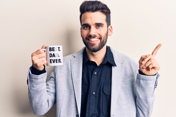 Young handsome man with beard drinking mug of coffe with best dad ever message smiling happy...