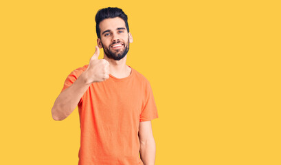Young handsome man with beard wearing casual t-shirt doing happy thumbs up gesture with hand. approving expression looking at the camera showing success.