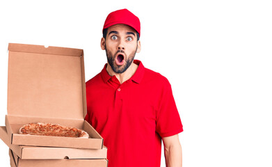 Young handsome man with beard wearing delivery uniform holding boxes with pizza scared and amazed with open mouth for surprise, disbelief face