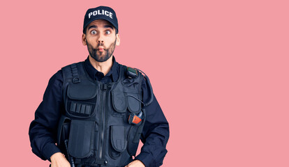 Young handsome man with beard wearing police uniform making fish face with lips, crazy and comical gesture. funny expression.