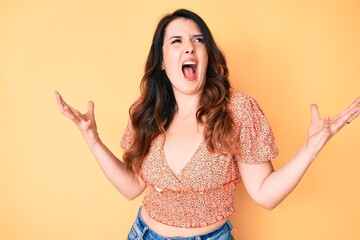 Young beautiful brunette woman wearing casual summer clothes crazy and mad shouting and yelling with aggressive expression and arms raised. frustration concept.