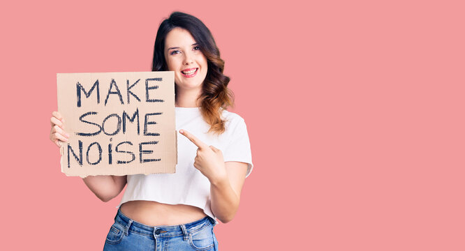 Beautiful young brunette woman holding make some noise banner smiling happy pointing with hand and finger