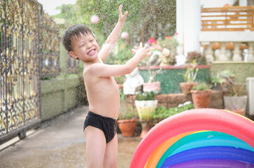 Obraz premium Cute little smiling Asian 4 - 5 years old toddler boy child having fun playing with splash water in the garden at home in the sunny morning, Hot summer day concept