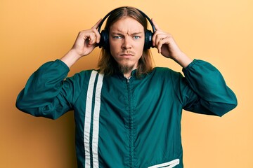 Handsome caucasian man with long hair wearing gym clothes and using headphones skeptic and nervous, frowning upset because of problem. negative person.