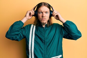 Handsome caucasian man with long hair wearing gym clothes and using headphones skeptic and nervous,...