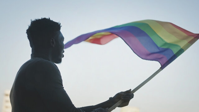 Black man waving rainbow flag symbols amid protesters for LGBT rights, pride events. High quality photo