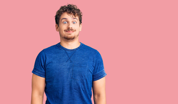 Young handsome man with curly hair wearing casual clothes puffing cheeks with funny face. mouth inflated with air, crazy expression.