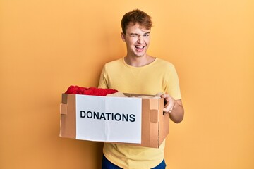 Young caucasian man holding donations box for charity winking looking at the camera with sexy...