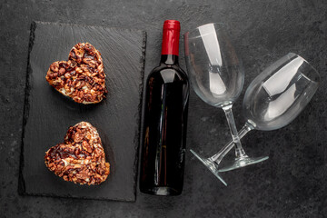 Two heart shaped cakes with walnuts and a bottle of wine with glasses on a stone background for valentine's day