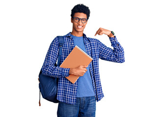 Young african american man wearing student backpack holding book looking confident with smile on face, pointing oneself with fingers proud and happy.