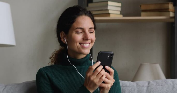 30s woman in earphones hold smart phone listen audio messages texting to friend, spend free time at home using modern wireless tech, fast wi fi connection, hear music online, digital services concept
