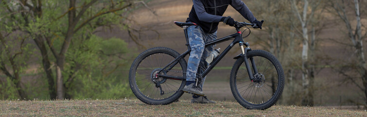 Fototapeta premium Sports brutal bearded guy on a modern mountain bike. Cyclist on the green hills in the spring.