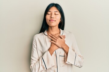 Young chinese woman wearing pajama smiling with hands on chest with closed eyes and grateful gesture on face. health concept.