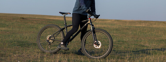 Fototapeta premium Cyclist in shorts and jersey on a modern carbon hardtail bike with an air suspension fork standing on a cliff against the background of fresh green spring forest