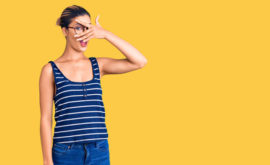 Young beautiful woman wearing casual clothes and glasses peeking in shock covering face and eyes with hand, looking through fingers with embarrassed expression.