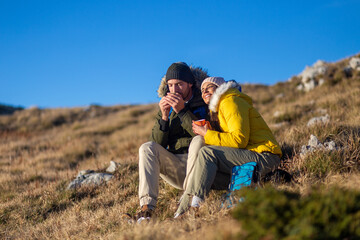 Happy couple drinking hot tea and enjoying the view at the top of the mountain.