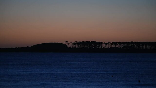 View of Gorriti Island at dusk, seen from Mansa Beach during a warm sunset. The shape of the trees can be seen in the horizon.