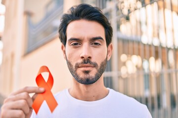 Young hispanic man with serious expression holding orange ribbon at the city. - obrazy, fototapety, plakaty