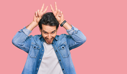 Young hispanic man wearing casual clothes posing funny and crazy with fingers on head as bunny ears, smiling cheerful