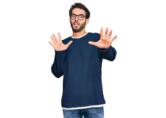 Young hispanic man wearing casual clothes and glasses afraid and terrified with fear expression stop gesture with hands, shouting in shock. panic concept.