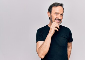 Middle age man wearing casual black t-shirt standing over isolated white background smiling looking confident at the camera with crossed arms and hand on chin. Thinking positive.