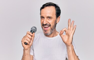 Middle age handsome singer man singing using microphone over isolated white background doing ok sign with fingers, smiling friendly gesturing excellent symbol