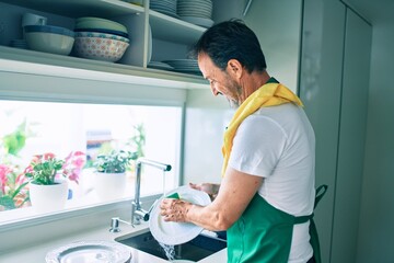 Middle age man with beard smiling happy washing dishes at home