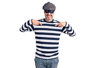 Middle age handsome man wearing burglar mask looking confident with smile on face, pointing oneself with fingers proud and happy.