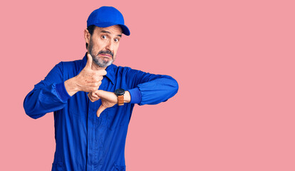 Middle age handsome man wearing mechanic uniform doing thumbs up and down, disagreement and agreement expression. crazy conflict